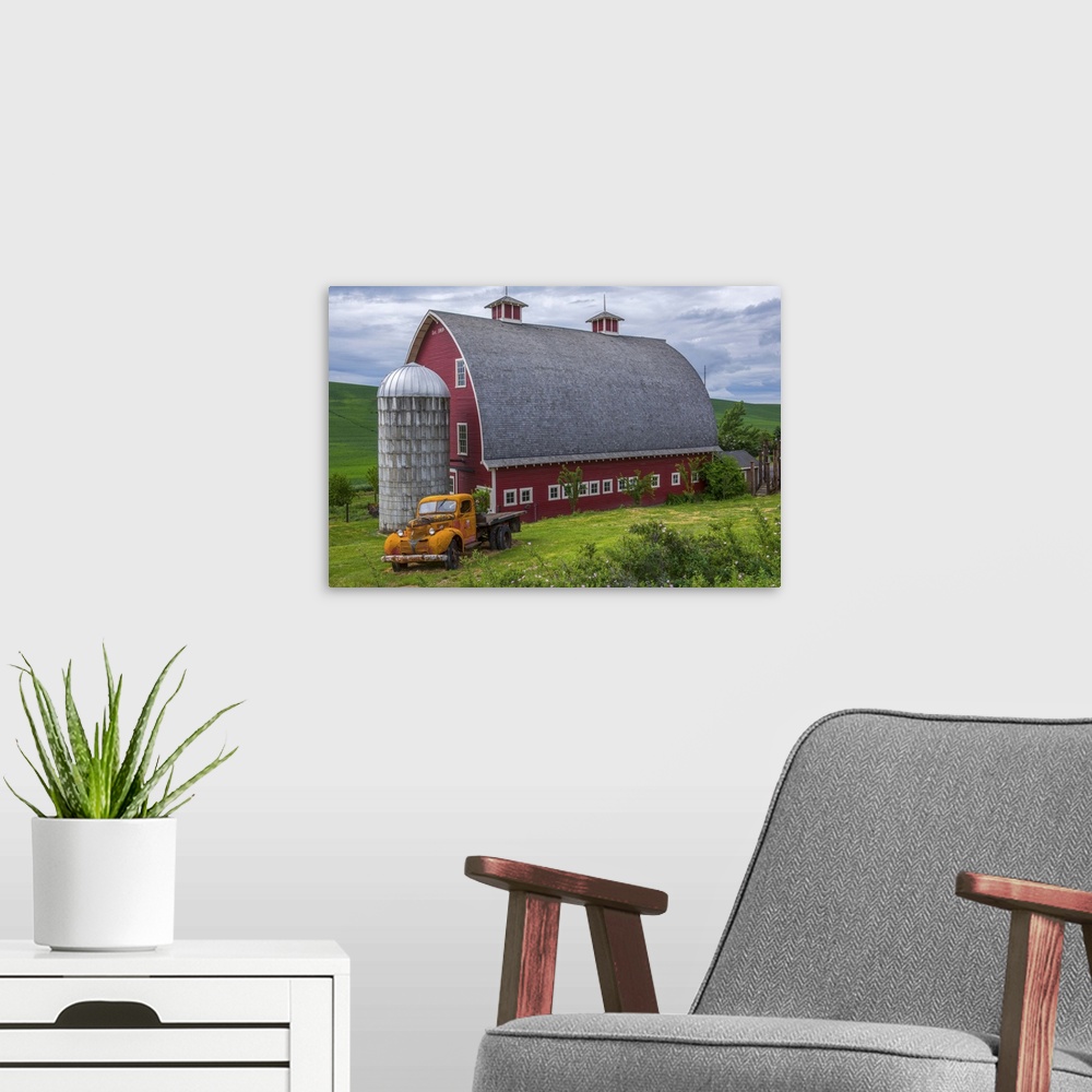 A modern room featuring A large red barn and an orange truck against the green landscape of Palouse, Washington.