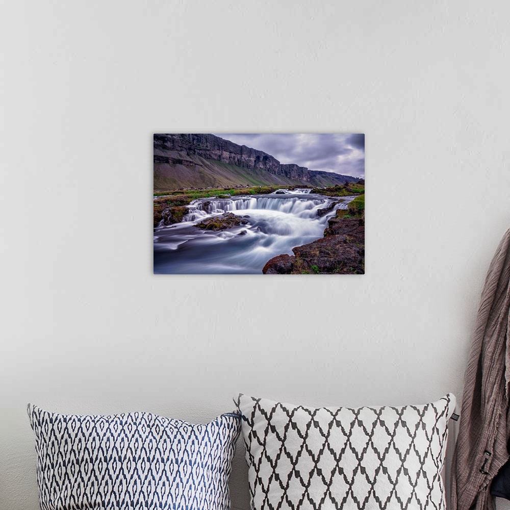 A bohemian room featuring Rushing water in a freezing river under a cloudy sky in Iceland.