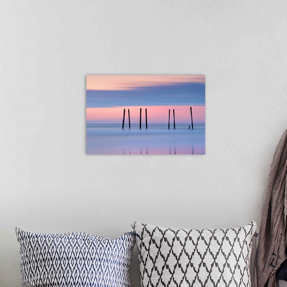 A bohemian room featuring Silhouettes of seven pilings in the ocean at sunset in New Jersey.