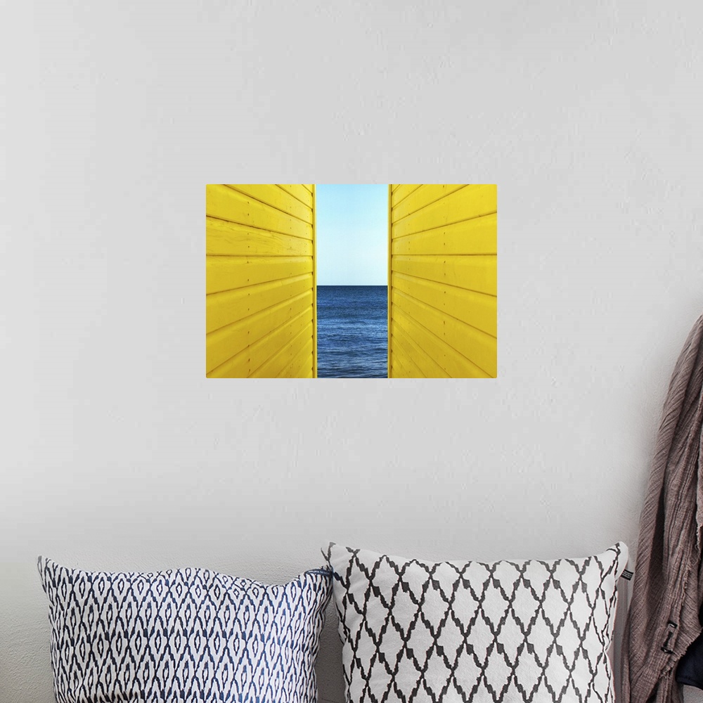 A bohemian room featuring Symetrical perspective of 2 Yellow Beach Huts with blue sky and sea inbetween them.