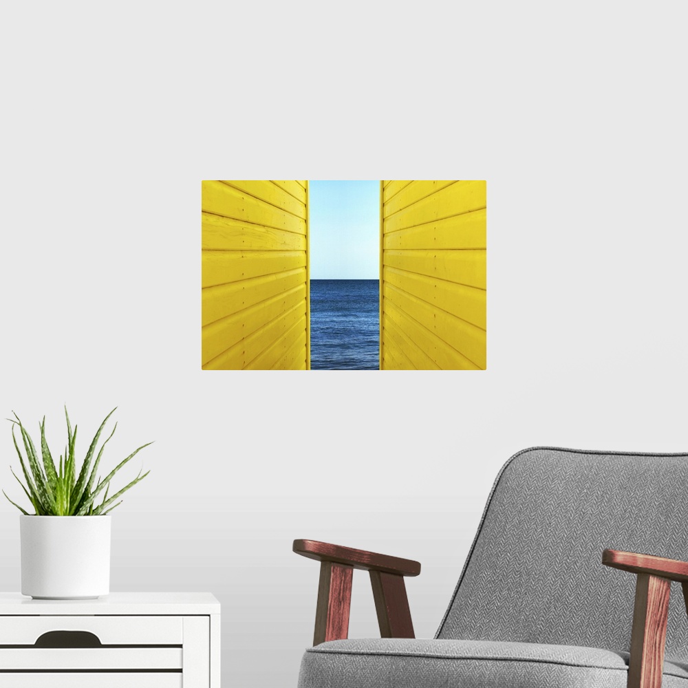 A modern room featuring Symetrical perspective of 2 Yellow Beach Huts with blue sky and sea inbetween them.