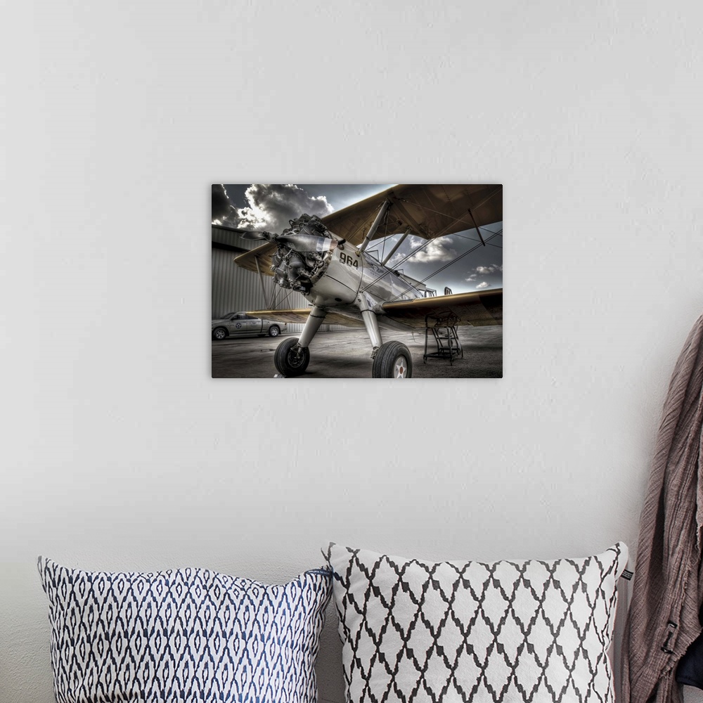 A bohemian room featuring A HDR photograph of a vintage air craft parked on the tarmac outside a hanger and a sky full of l...
