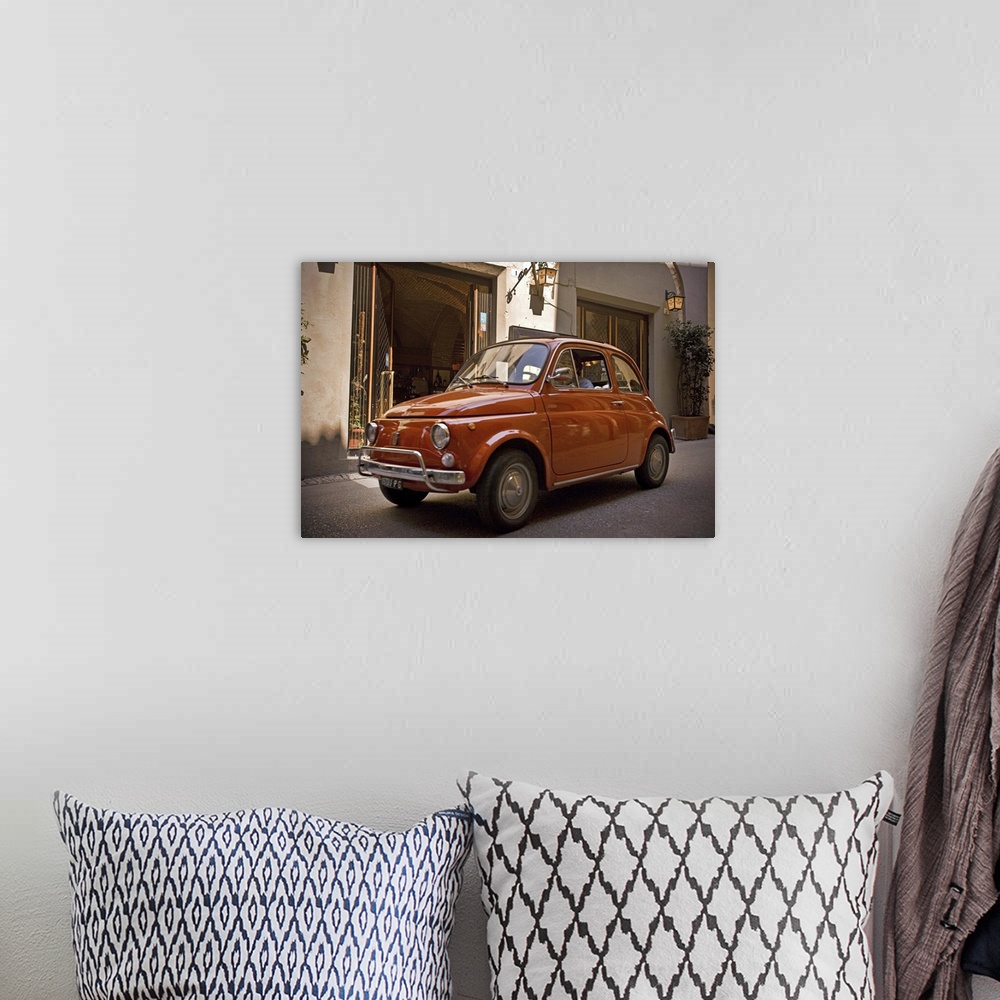 A bohemian room featuring A small red car drives through the narrow streets in the downtown area of an Italian city.
