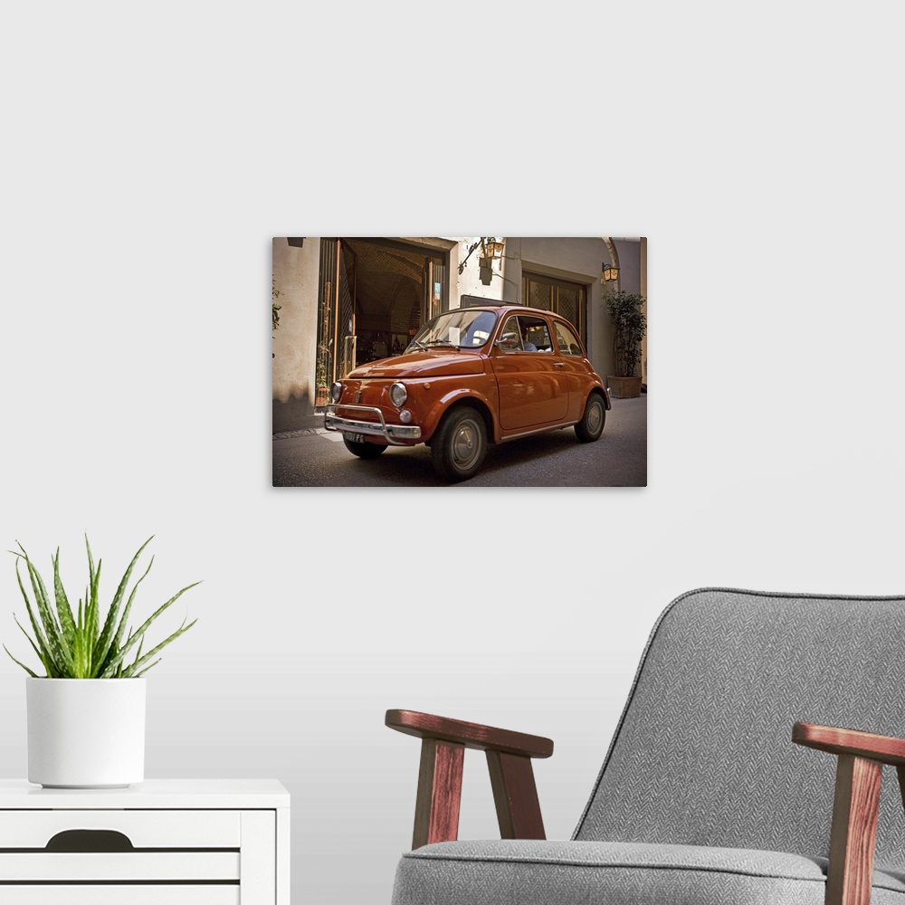 A modern room featuring A small red car drives through the narrow streets in the downtown area of an Italian city.