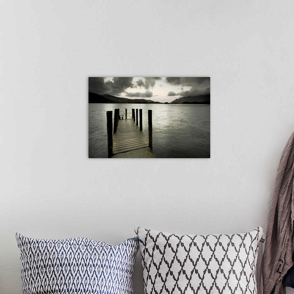 A bohemian room featuring A small wooden jetty looking out over a lake with stormy clouds over a dark headland