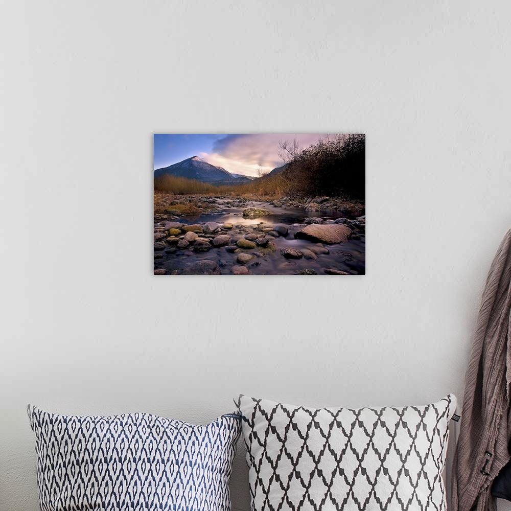 A bohemian room featuring A rocky river overlooking a mountain at sunset.