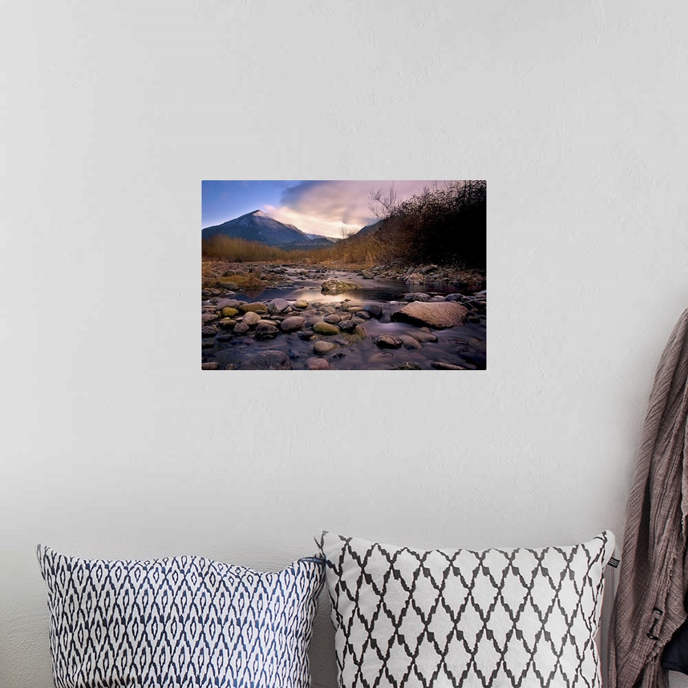 A bohemian room featuring A rocky river overlooking a mountain at sunset.