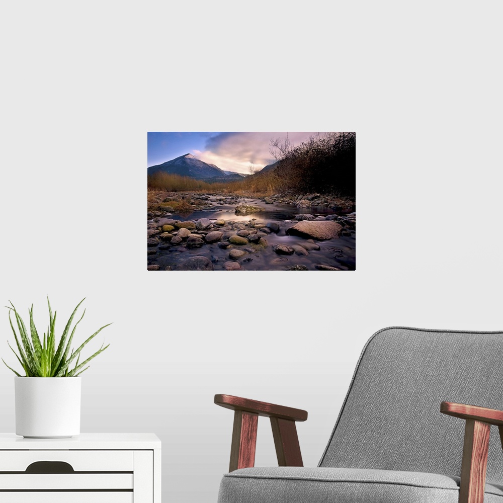 A modern room featuring A rocky river overlooking a mountain at sunset.