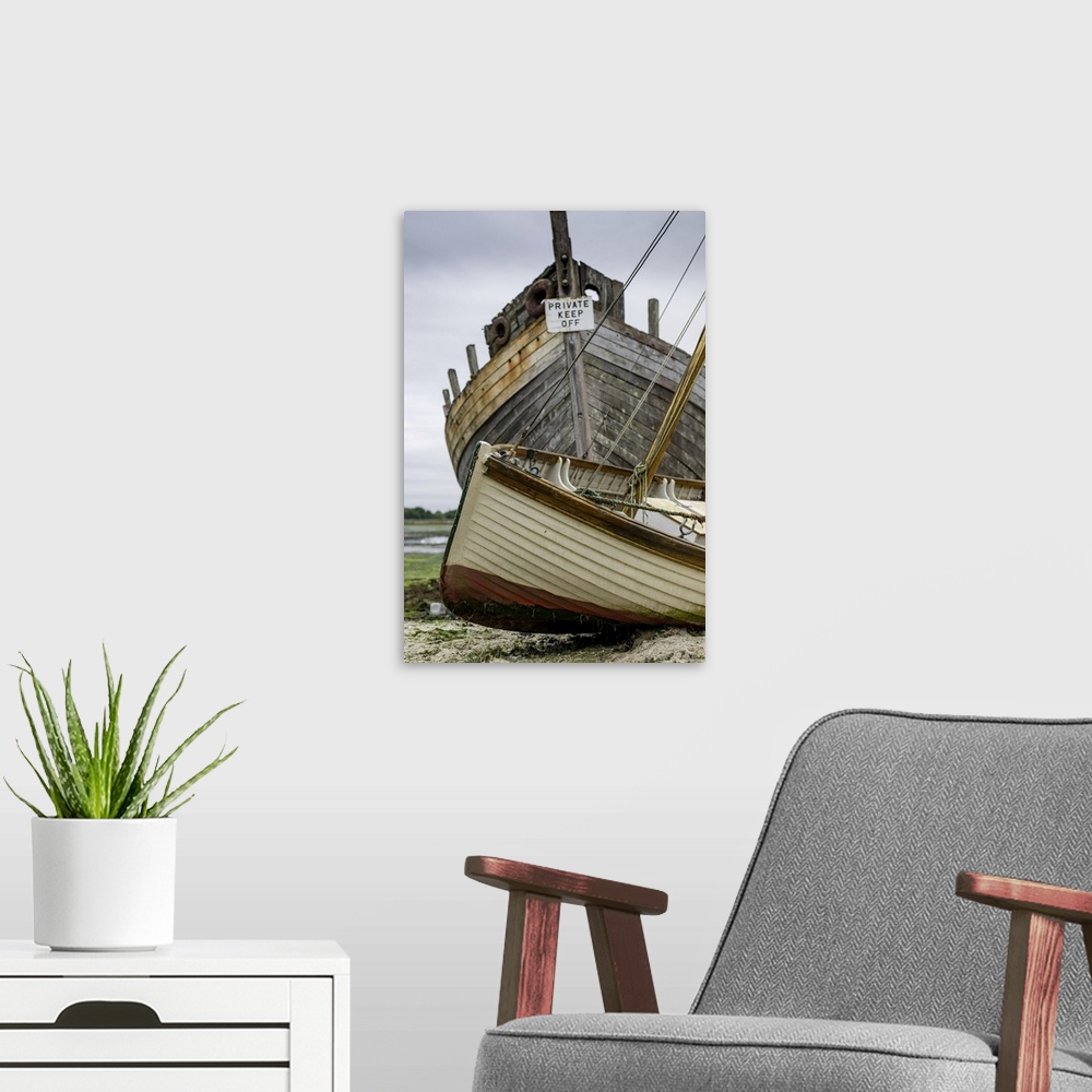 A modern room featuring A small sailing dinghy beside a large rotting hulk of a boat.