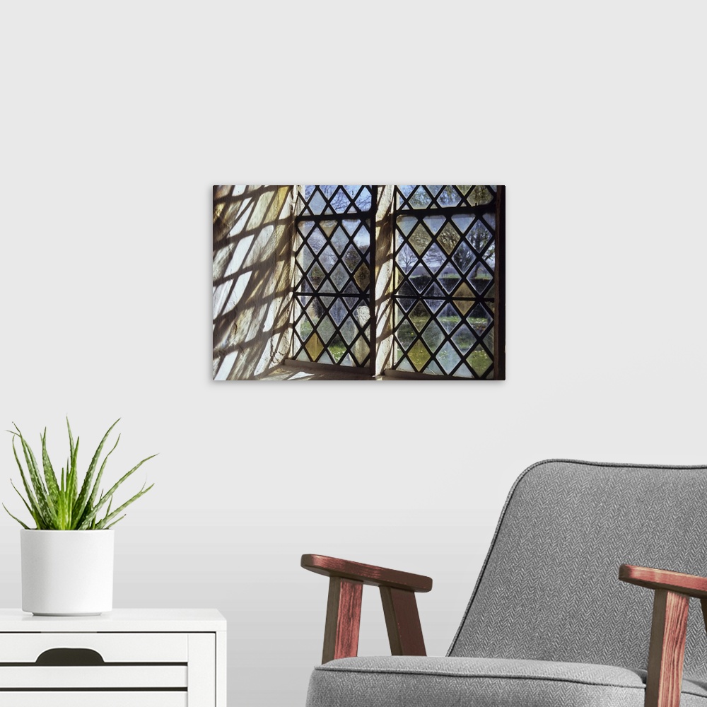 A modern room featuring Detail of stone-framed church window with diamond-leaded panes of clear or pale yellow glass thro...