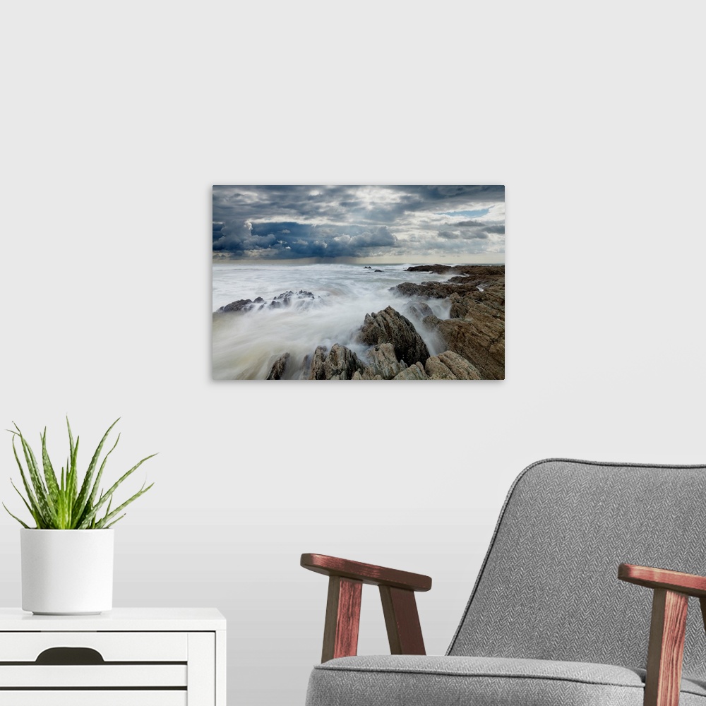 A modern room featuring Jagged rocks on coastline with white surf under grey storm clouds