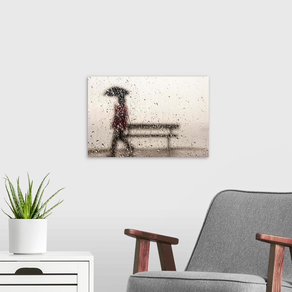 A modern room featuring A man walking with an umbrella against a rain streaked window.