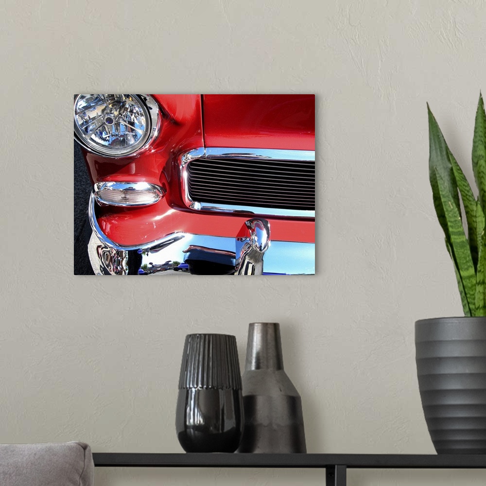 A modern room featuring The front of a red car with shiny chrome bumper and grill