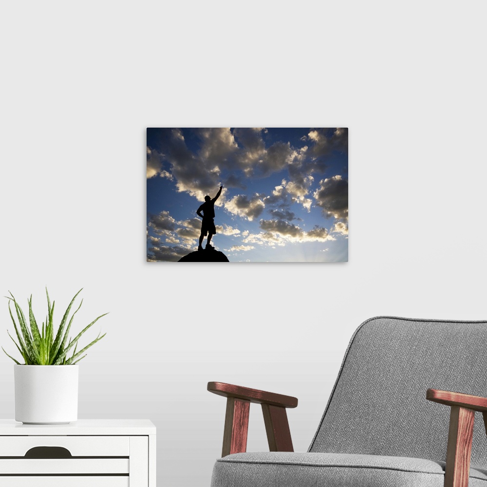 A modern room featuring man standing on pinnacle looking on with confidence as the sun sets with arm raised and fist clen...