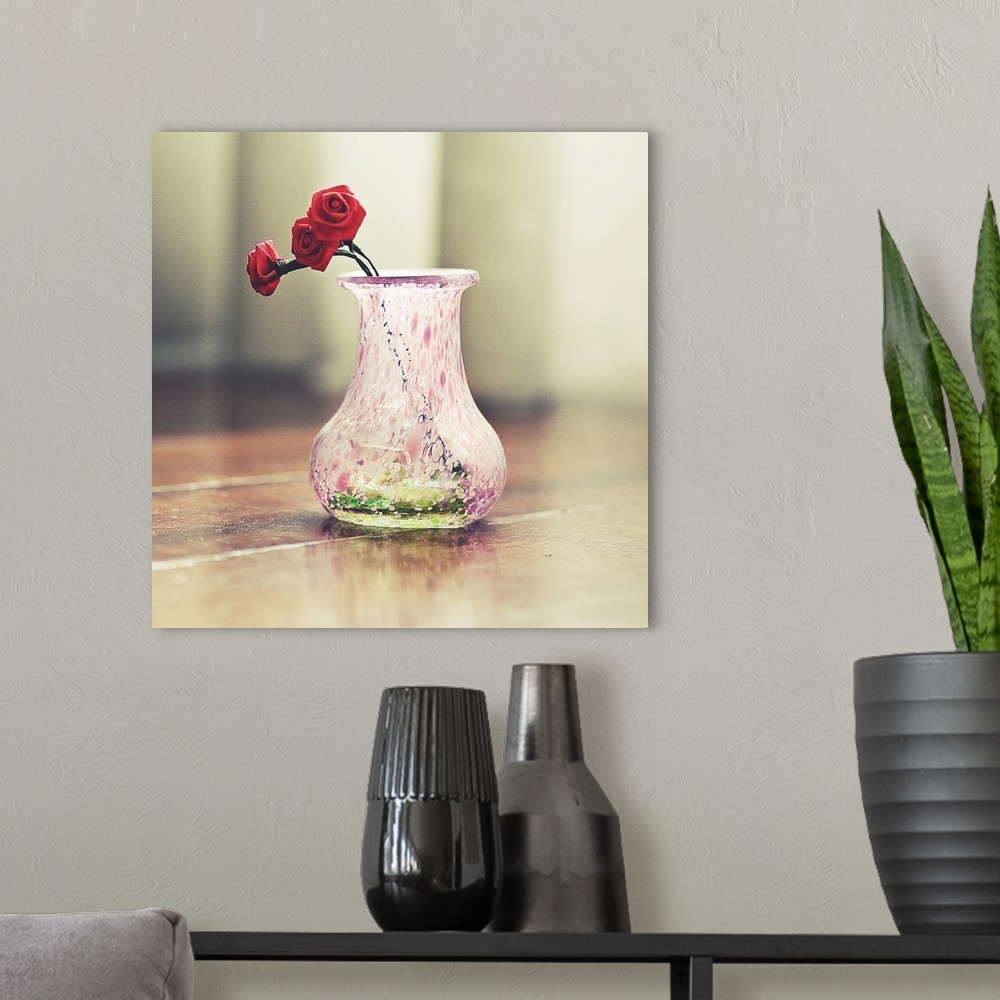 A modern room featuring Close up of a decorated small pink pitcher with three red roses made of cloth inside.