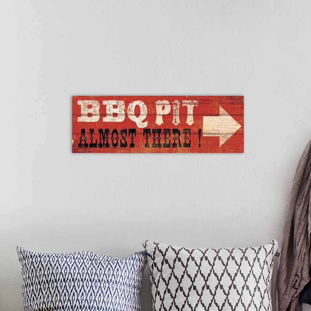 A bohemian room featuring This art piece resembles wood planks with an arrow and text painted saying BBQ Pit, Almost There.