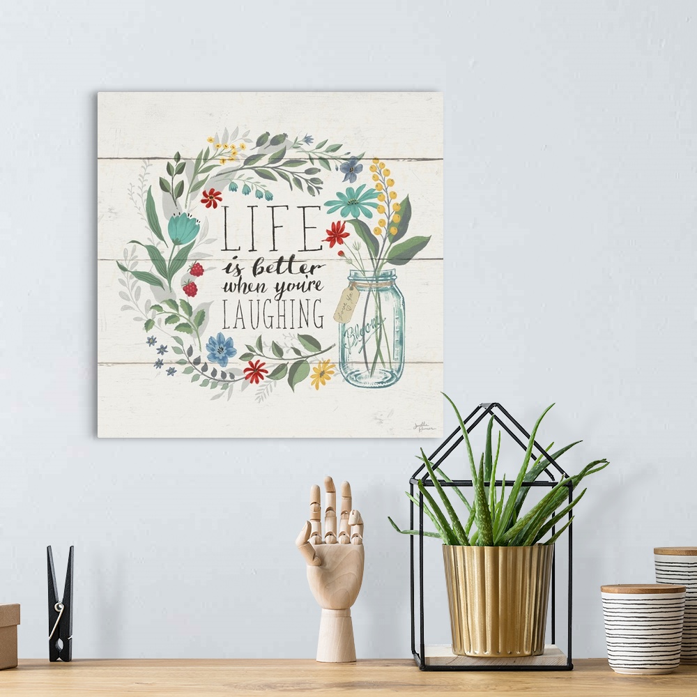 A bohemian room featuring "Life is Better When You're Laughing" written inside a floral wreath on a white wood paneled back...