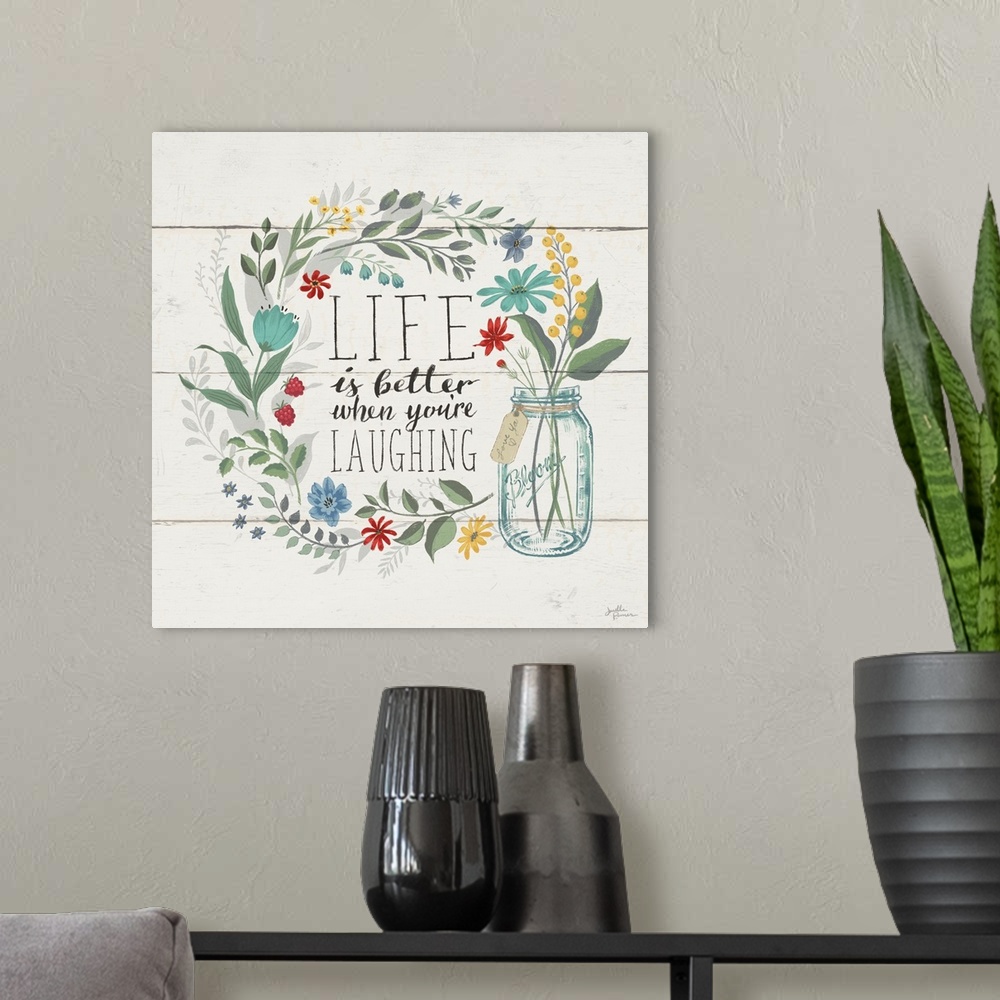 A modern room featuring "Life is Better When You're Laughing" written inside a floral wreath on a white wood paneled back...