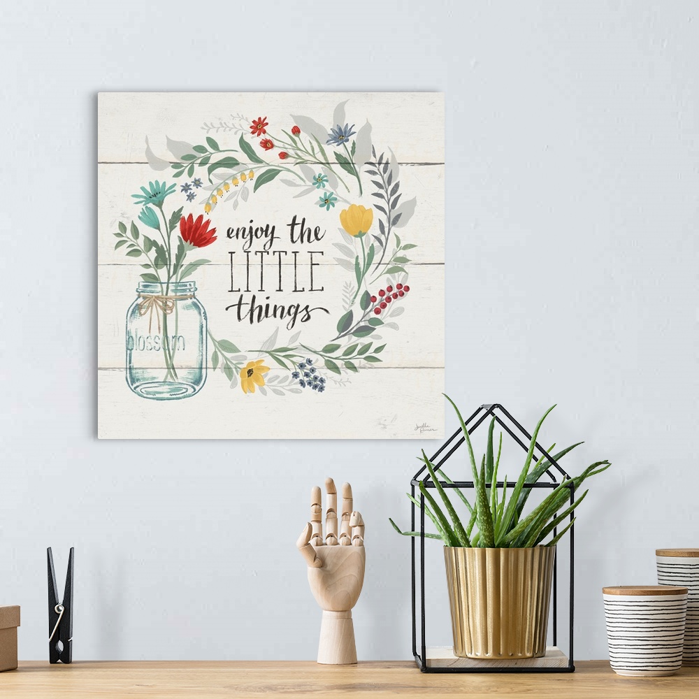 A bohemian room featuring "Enjoy the Little Things" written inside a floral wreath on a white wood paneled background.