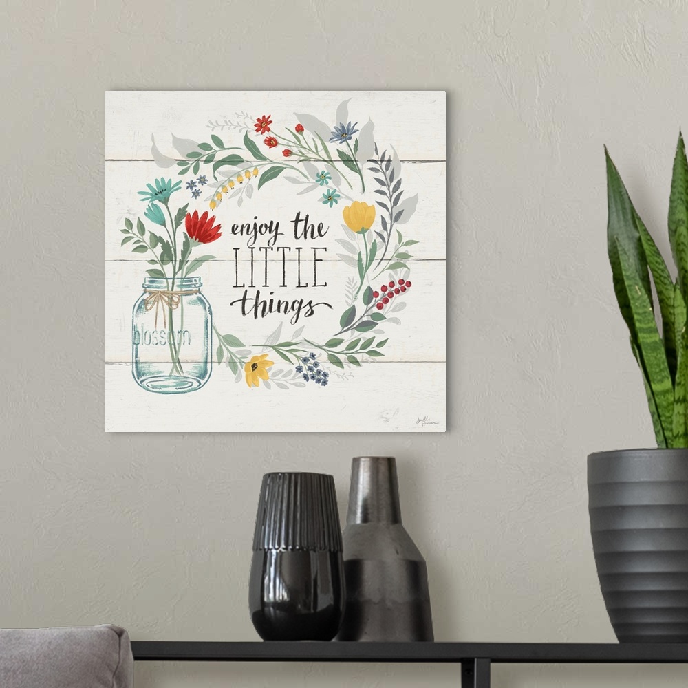 A modern room featuring "Enjoy the Little Things" written inside a floral wreath on a white wood paneled background.