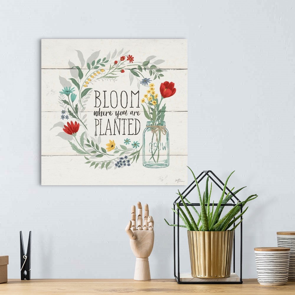 A bohemian room featuring "Bloom Where You Are Planted" written inside a floral wreath on a white wood paneled background.