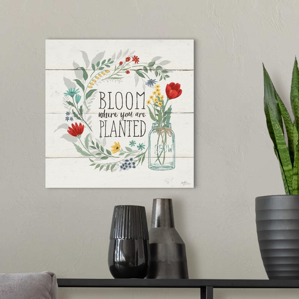 A modern room featuring "Bloom Where You Are Planted" written inside a floral wreath on a white wood paneled background.