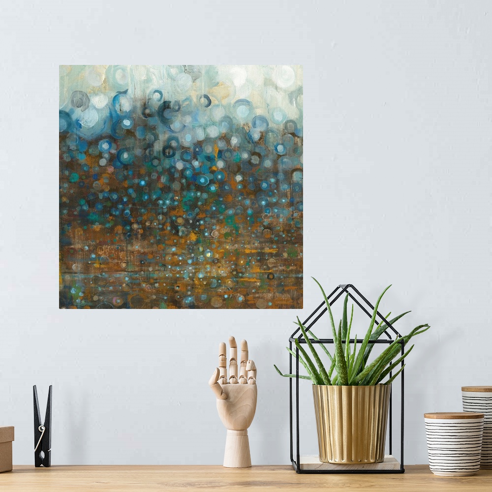 A bohemian room featuring Square abstract painting with a bronze background that has different shades of blue circles falli...