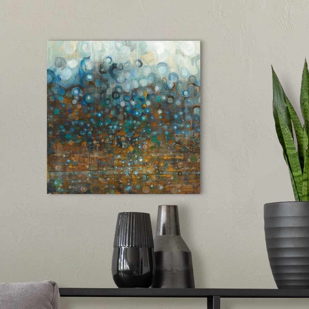 A modern room featuring Square abstract painting with a bronze background that has different shades of blue circles falli...