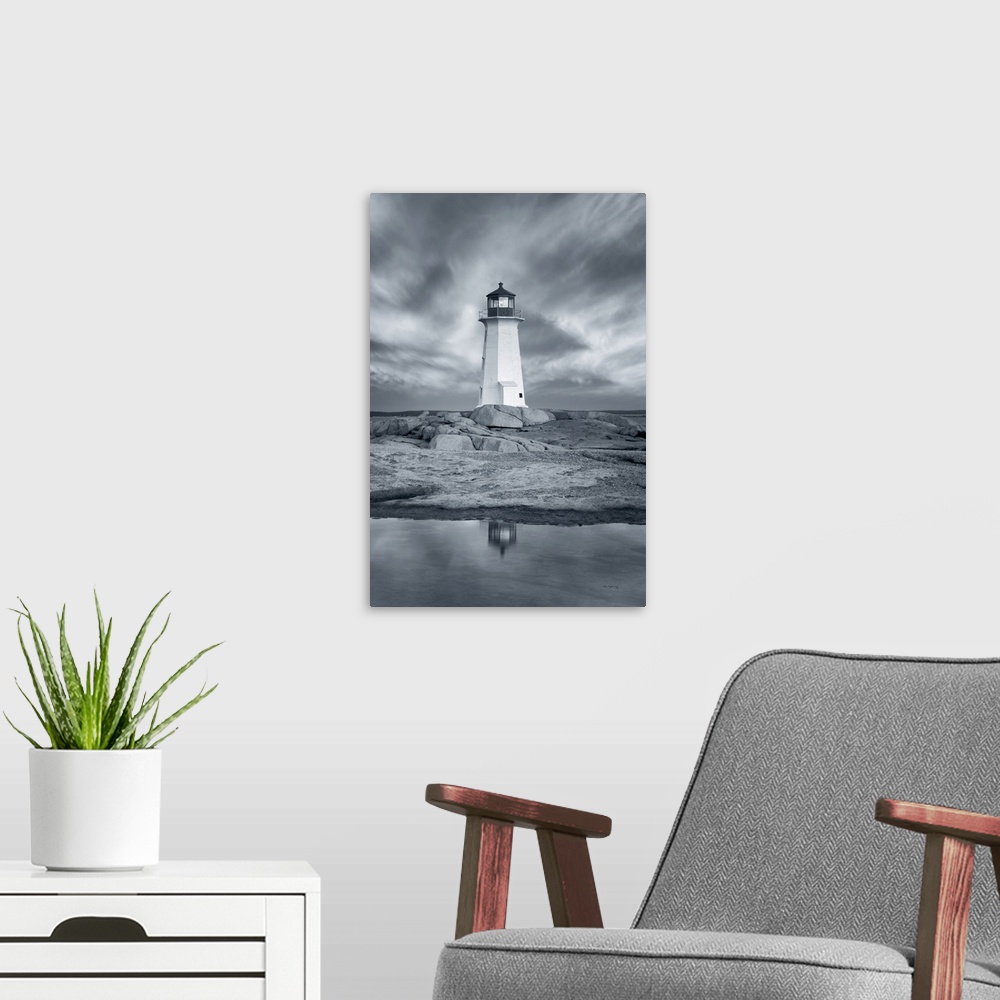 A modern room featuring A vertical black and white photograph of a white lighthouse reflecting in the water with a dramat...