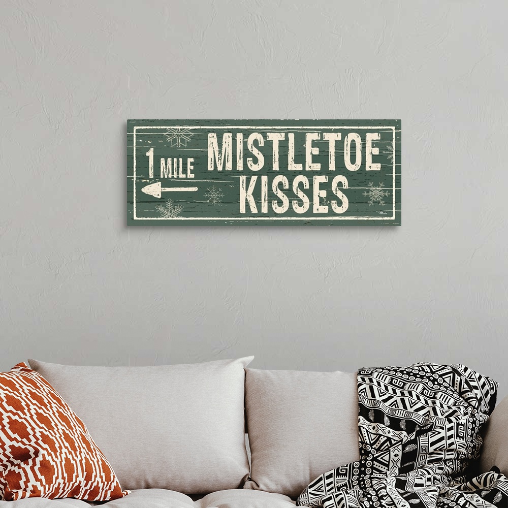 A bohemian room featuring Decorative artwork with a holiday theme with the text "1 Mile Mistletoe Kisses" on a green backdrop.