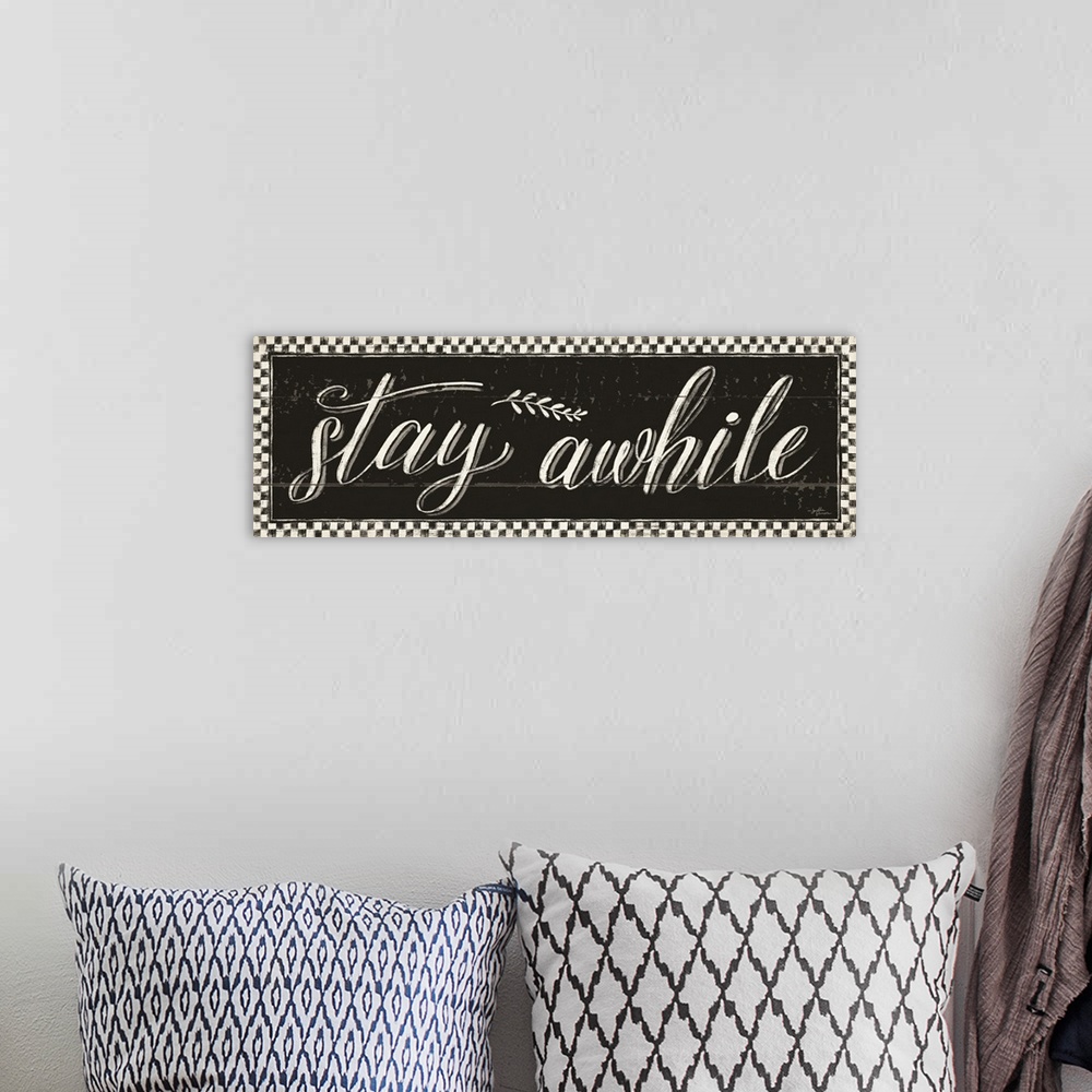 A bohemian room featuring Decorative artwork featuring the words, 'Stay awhile' on a distressed black background with a che...