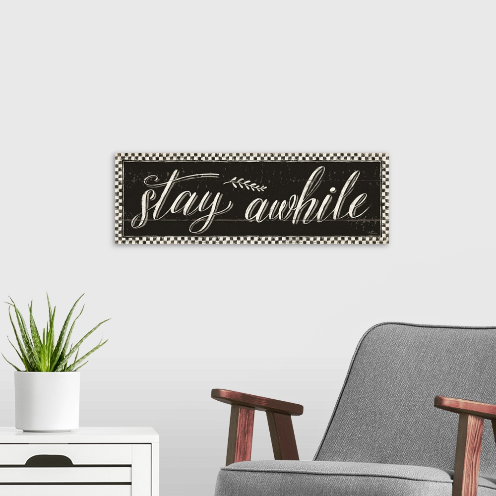 A modern room featuring Decorative artwork featuring the words, 'Stay awhile' on a distressed black background with a che...