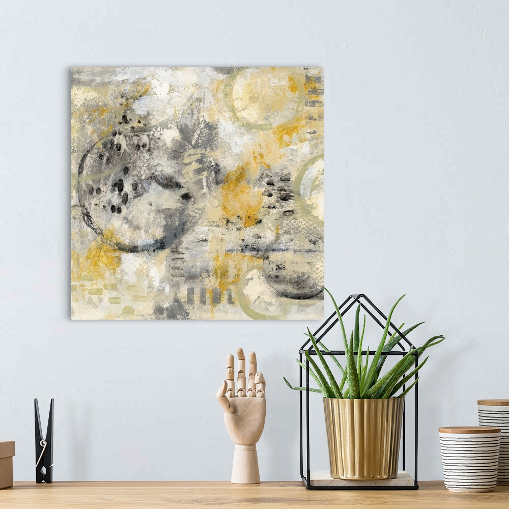 A bohemian room featuring Square abstract painting using gold, black, and grey hues with hidden circles sporadically around.