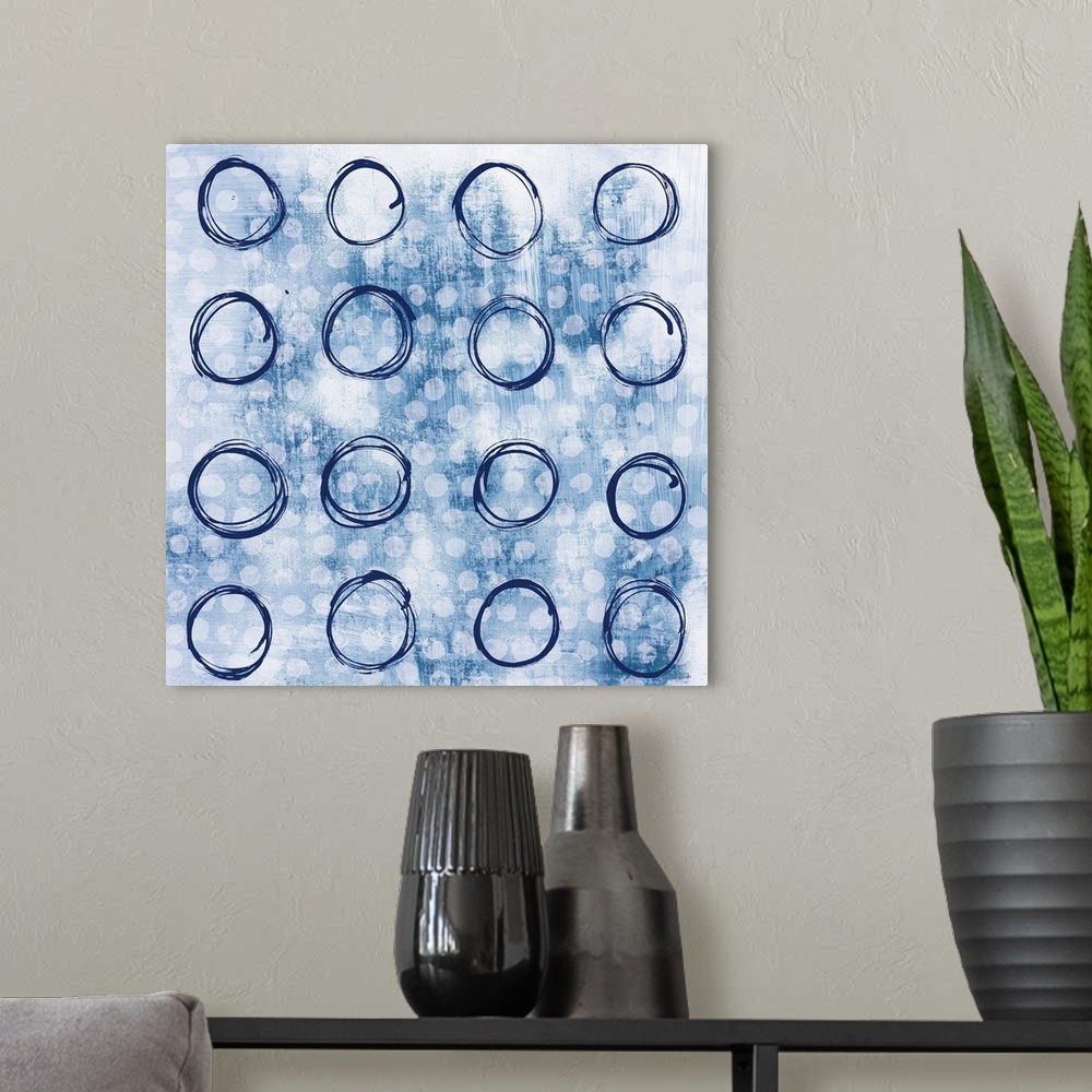 A modern room featuring Square abstract painting with indigo outlines of circles in rows in the foreground and smaller, s...