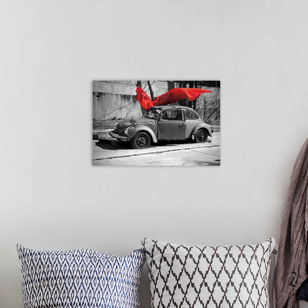 A bohemian room featuring A black and white photograph of a car with a colorized red cloth hanging in the air.