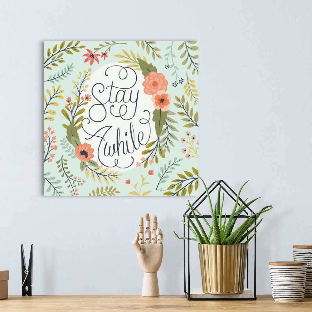 A bohemian room featuring "Stay Awhile" handwritten with loopy finishes, inside of a floral display on a mint colored backg...
