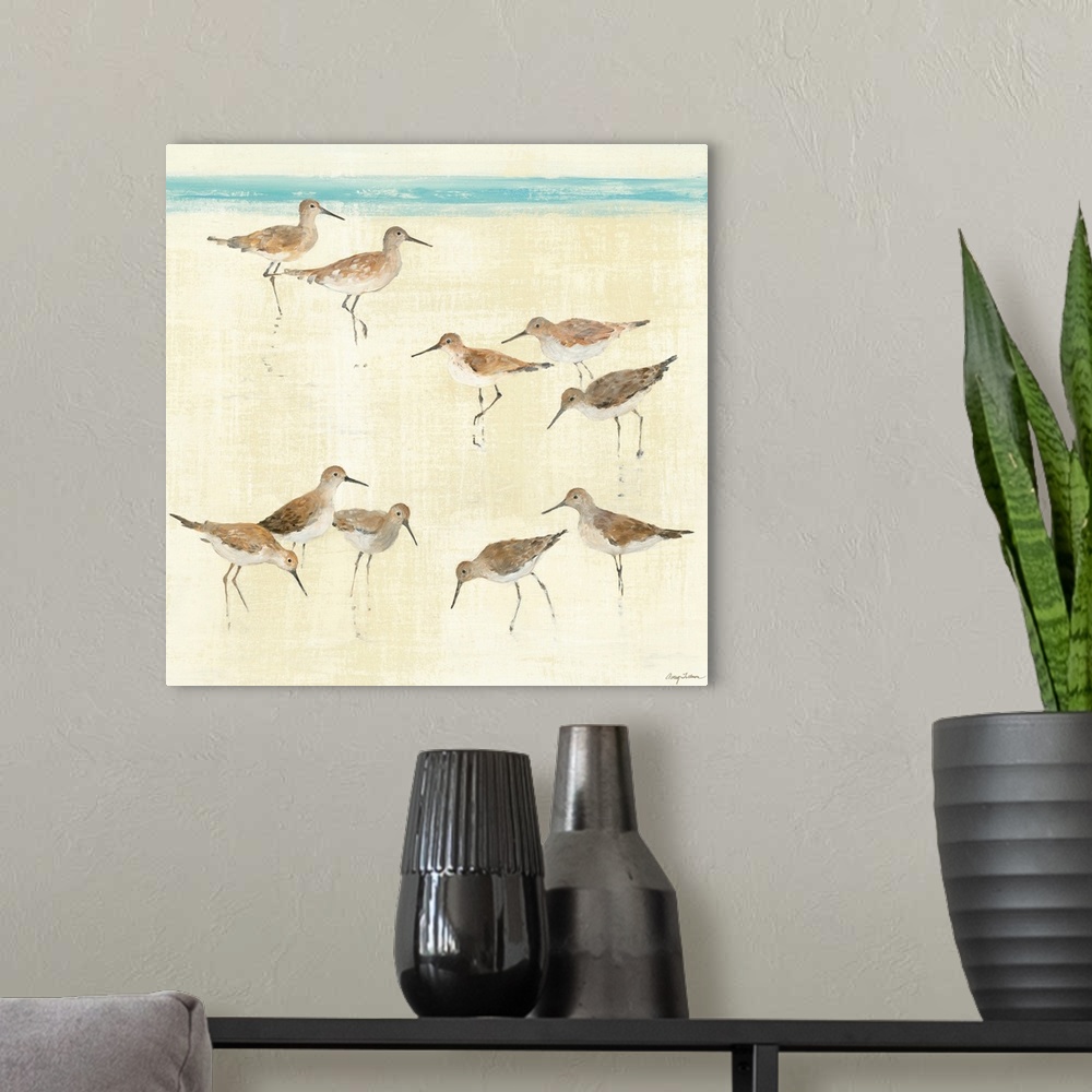 A modern room featuring Square, large artwork of a group of sandpiper birds standing on the beach, near the edge of blue ...