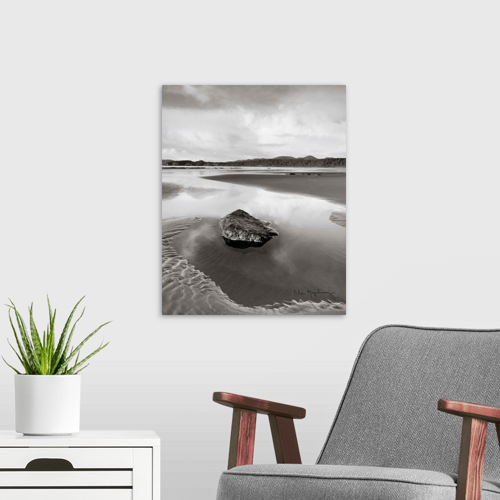A modern room featuring A black and white photograph of an idyllic beach scene, with a large rock in the foreground.