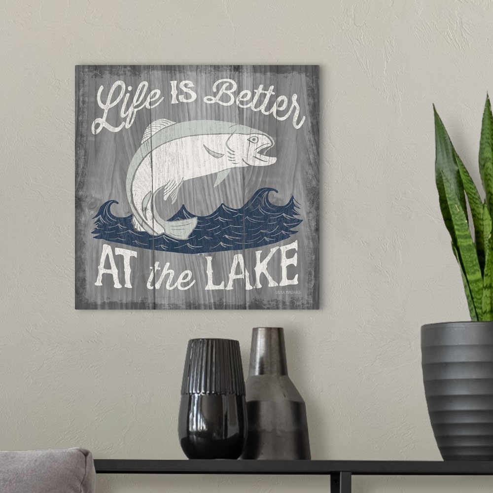 A modern room featuring "Life is Better at the Lake" in white with an illustration of a fish jumping out of water on a  g...