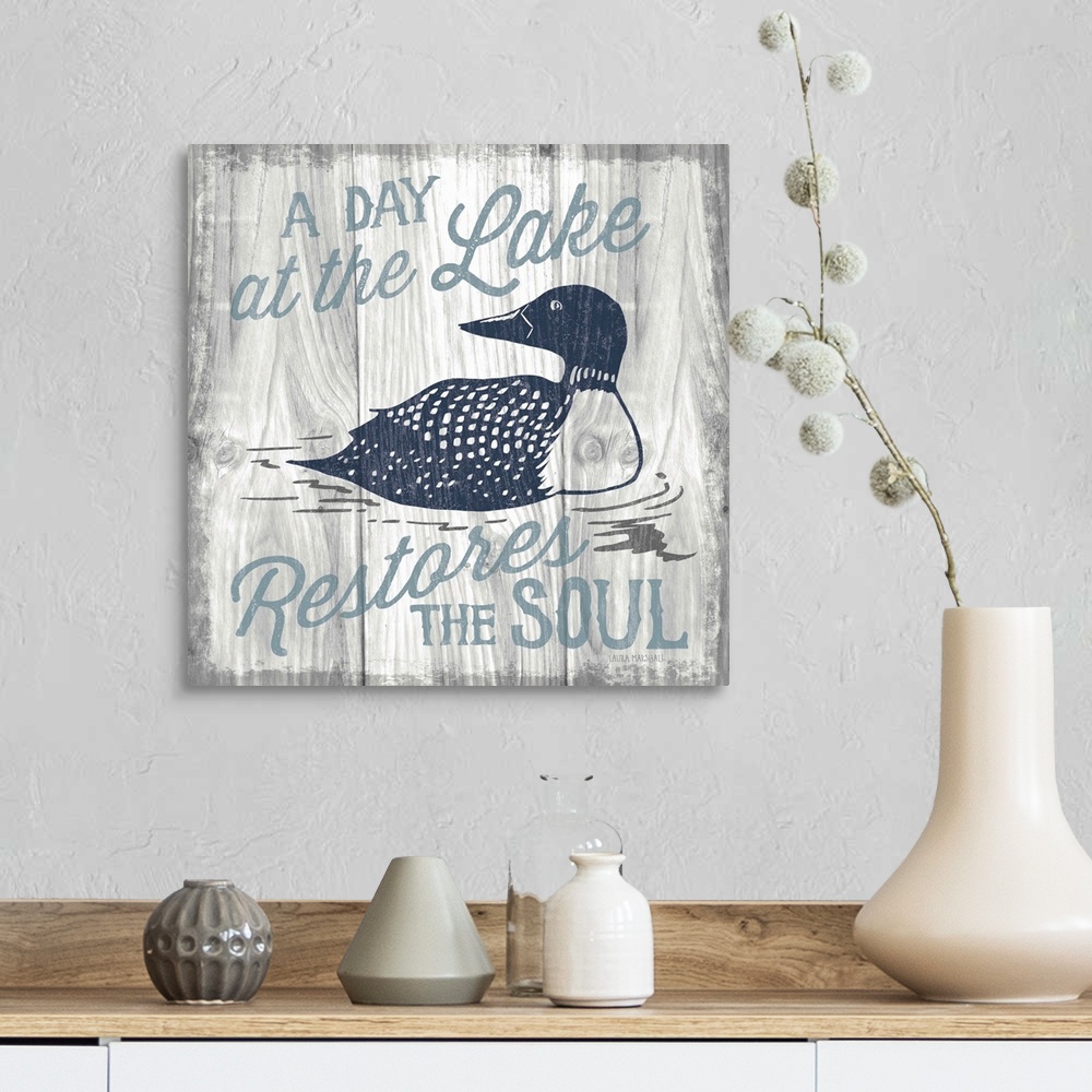 A farmhouse room featuring "A Day at the Lake Restores the Soul" in blue with an illustration of a duck on a grey wood grain...