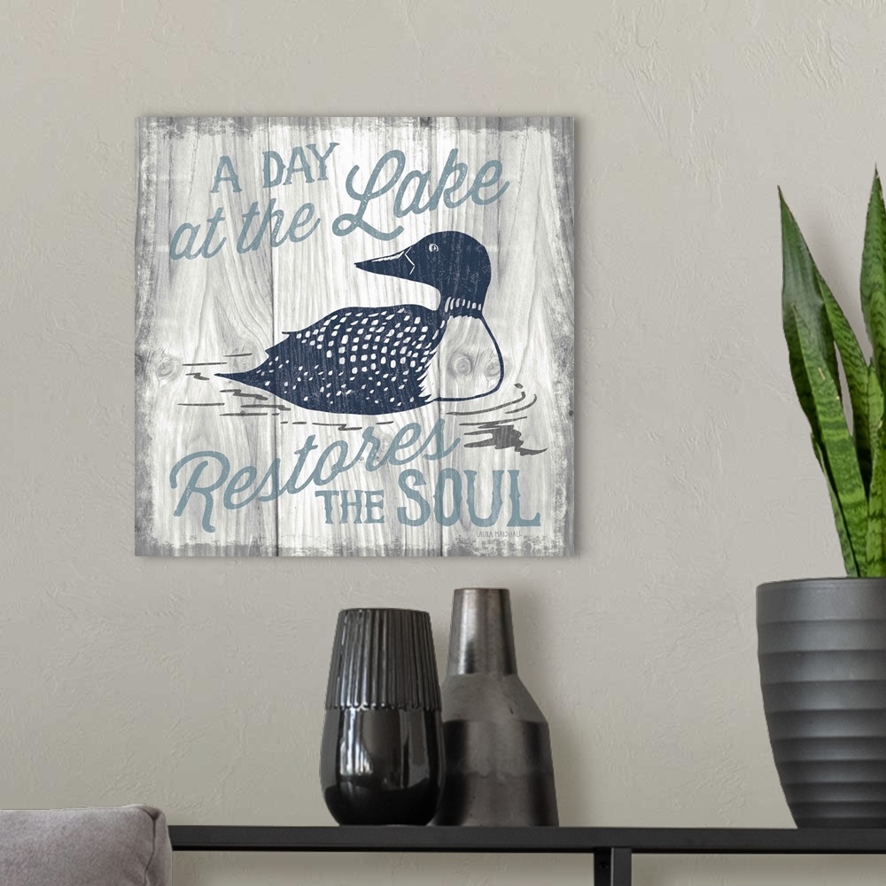 A modern room featuring "A Day at the Lake Restores the Soul" in blue with an illustration of a duck on a grey wood grain...