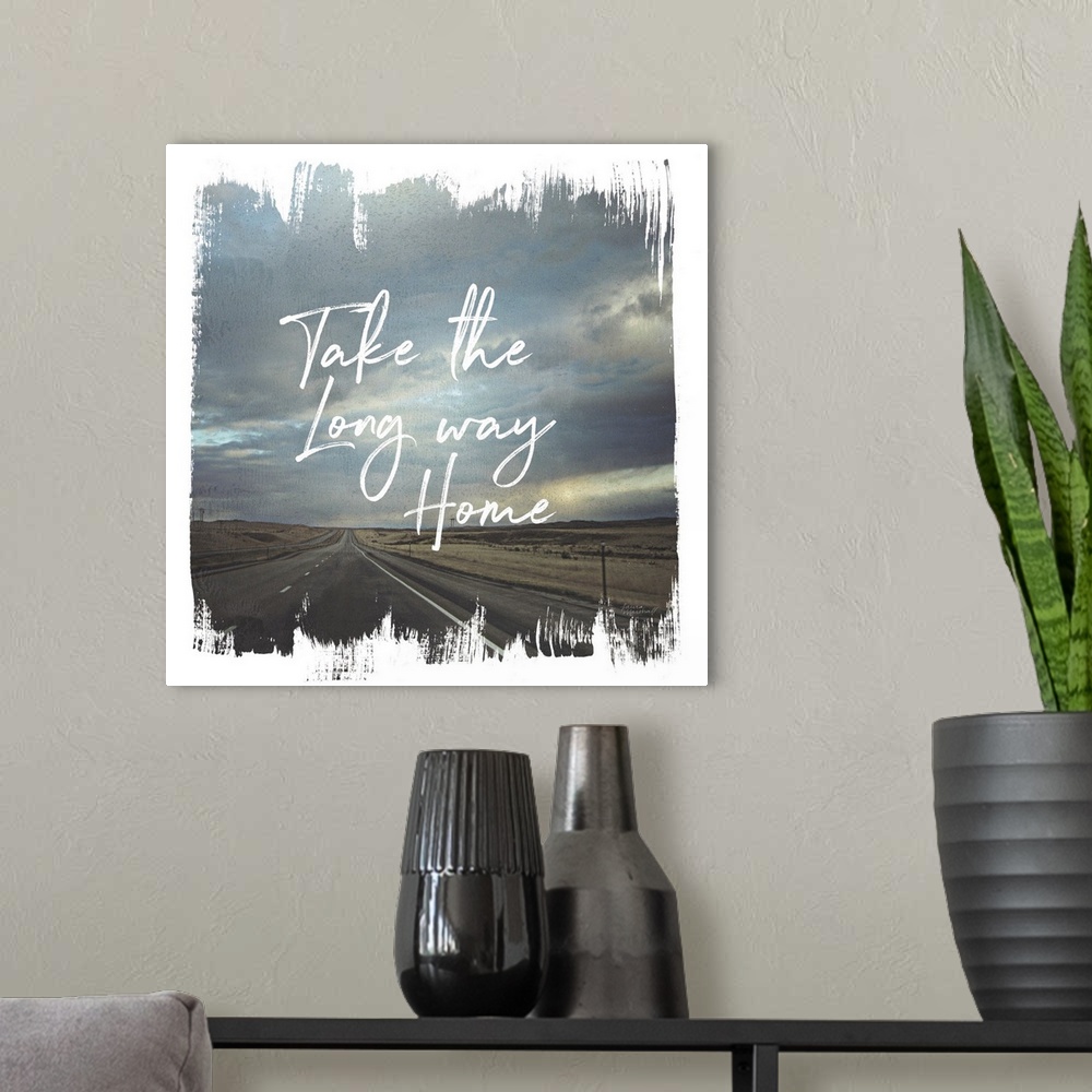 A modern room featuring "The the Long Way Home" written on top of a photograph of a long road and cloudy sky with brushst...
