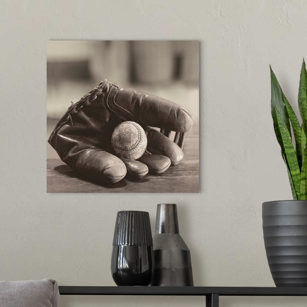 A modern room featuring Square sepia toned photograph of a worn baseball in a vintage mitt on a soft focus backdrop.