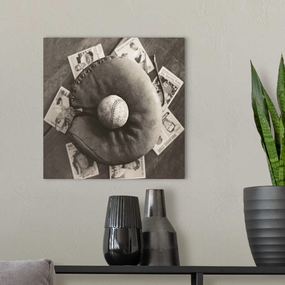 A modern room featuring Square sepia toned photograph of a worn baseball in an old mitt and vintage baseball cards behind...