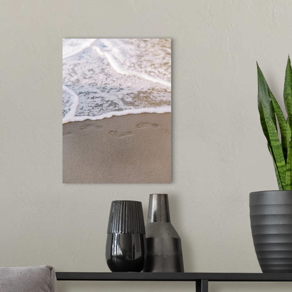 A modern room featuring A photograph of small footprints in the sand about to be lapped with gentle waves.