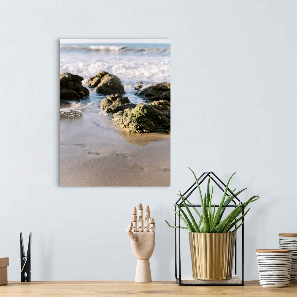 A bohemian room featuring A photograph of footprints in the sand at the edge of the ocean on a rocky beach.