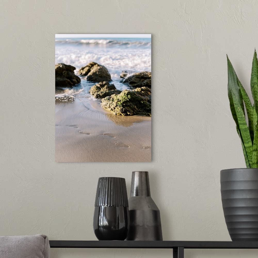 A modern room featuring A photograph of footprints in the sand at the edge of the ocean on a rocky beach.