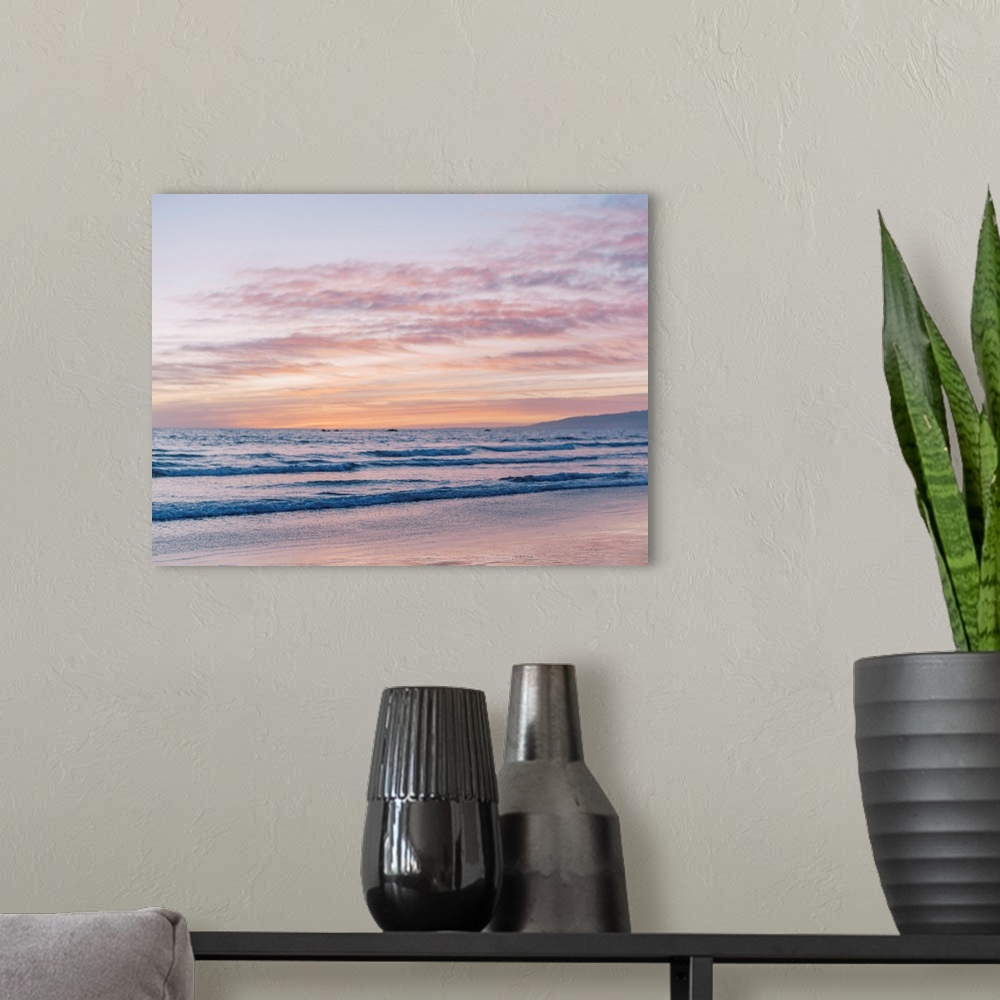 A modern room featuring A photograph of gentle waves lapping the beach under an early evening sky where the sun is beginn...