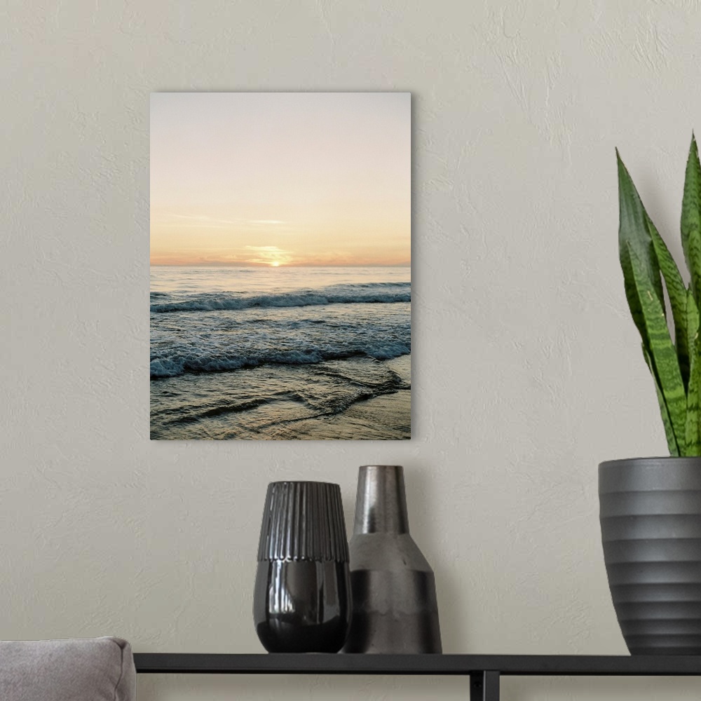 A modern room featuring A photograph of gentle waves lapping the beach under an early evening sky where the sun is beginn...