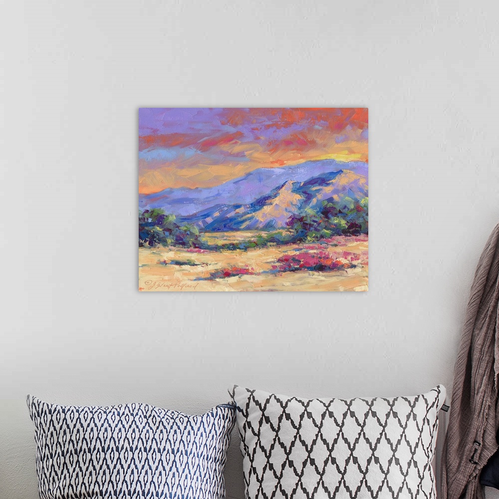 A bohemian room featuring Contemporary vibrant landscape painting of a desert mountain sunset.